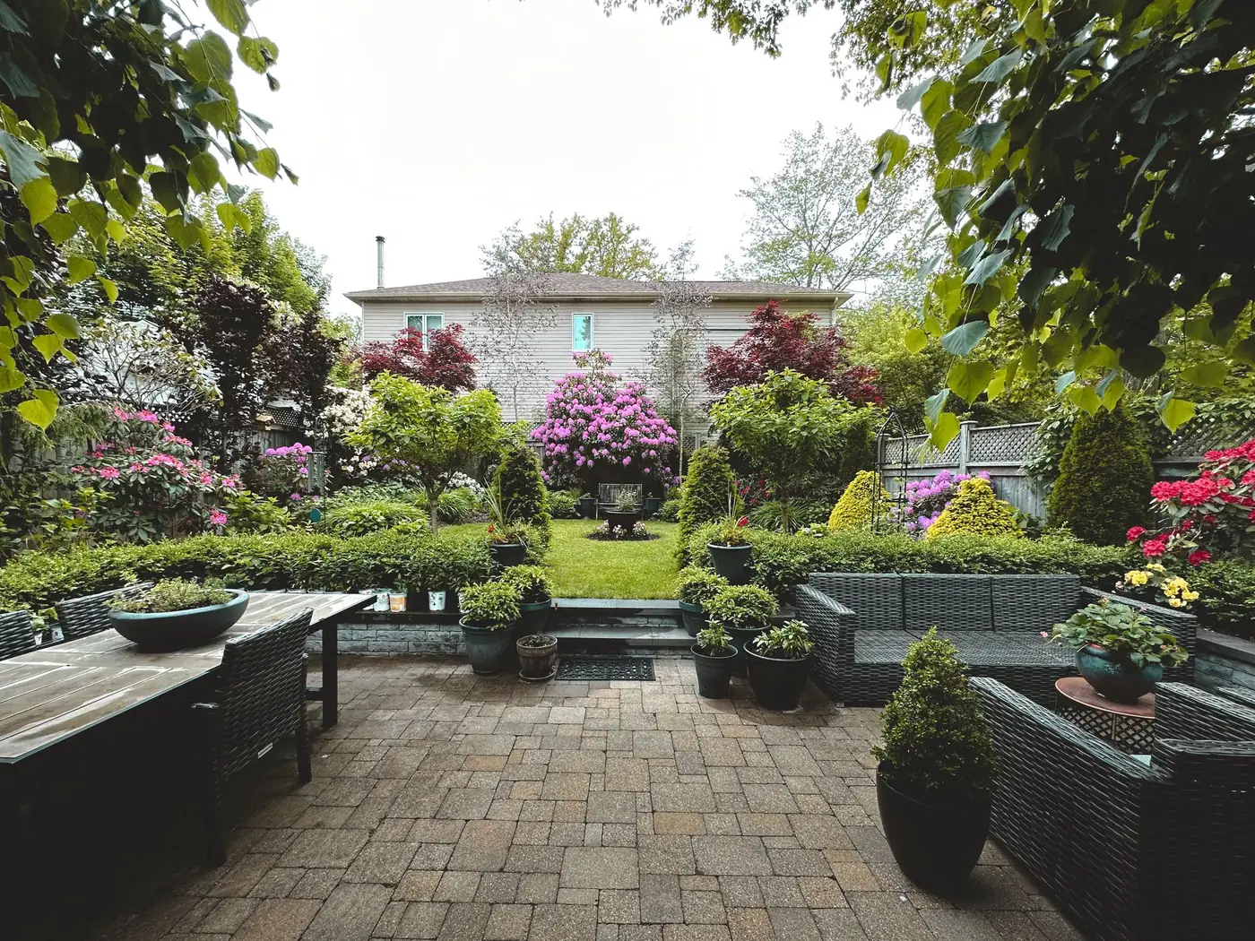 A paver patio framed by a lush, flowering backyard garden and manicured lawn